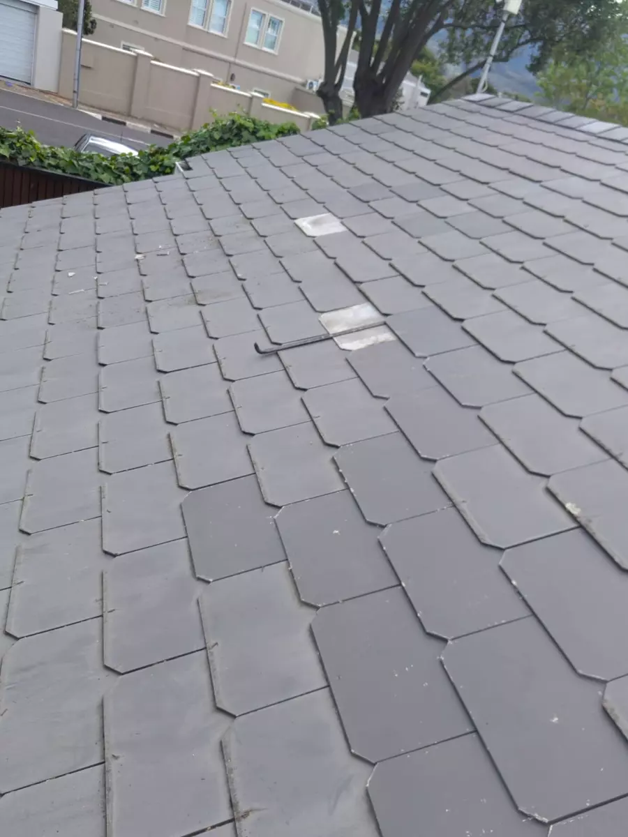 Grey slate roof tiles with damaged patches and a pipe